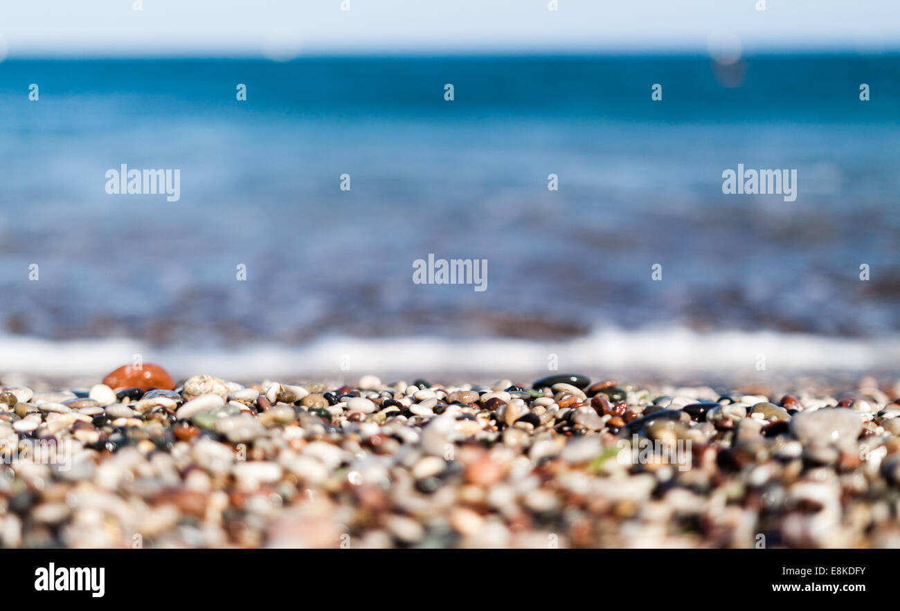 close up of a rocky beach with selective focus on blurry colorful rocky coast and blurry blue water in Faliraki Rhodes Island Stock Photo