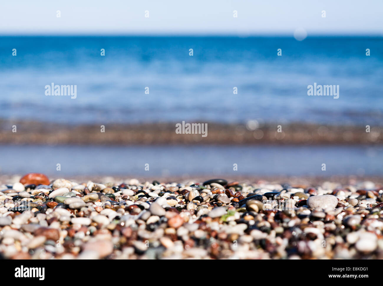 close up of a rocky beach with selective focus on blurry colorful rocky coast and blurry blue water in Faliraki Rhodes Island Stock Photo