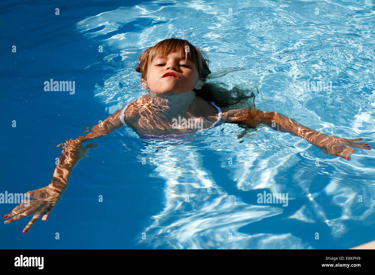 A 6-year old girl swimming for the first time without armbands in a swimming pool. Stock Photo