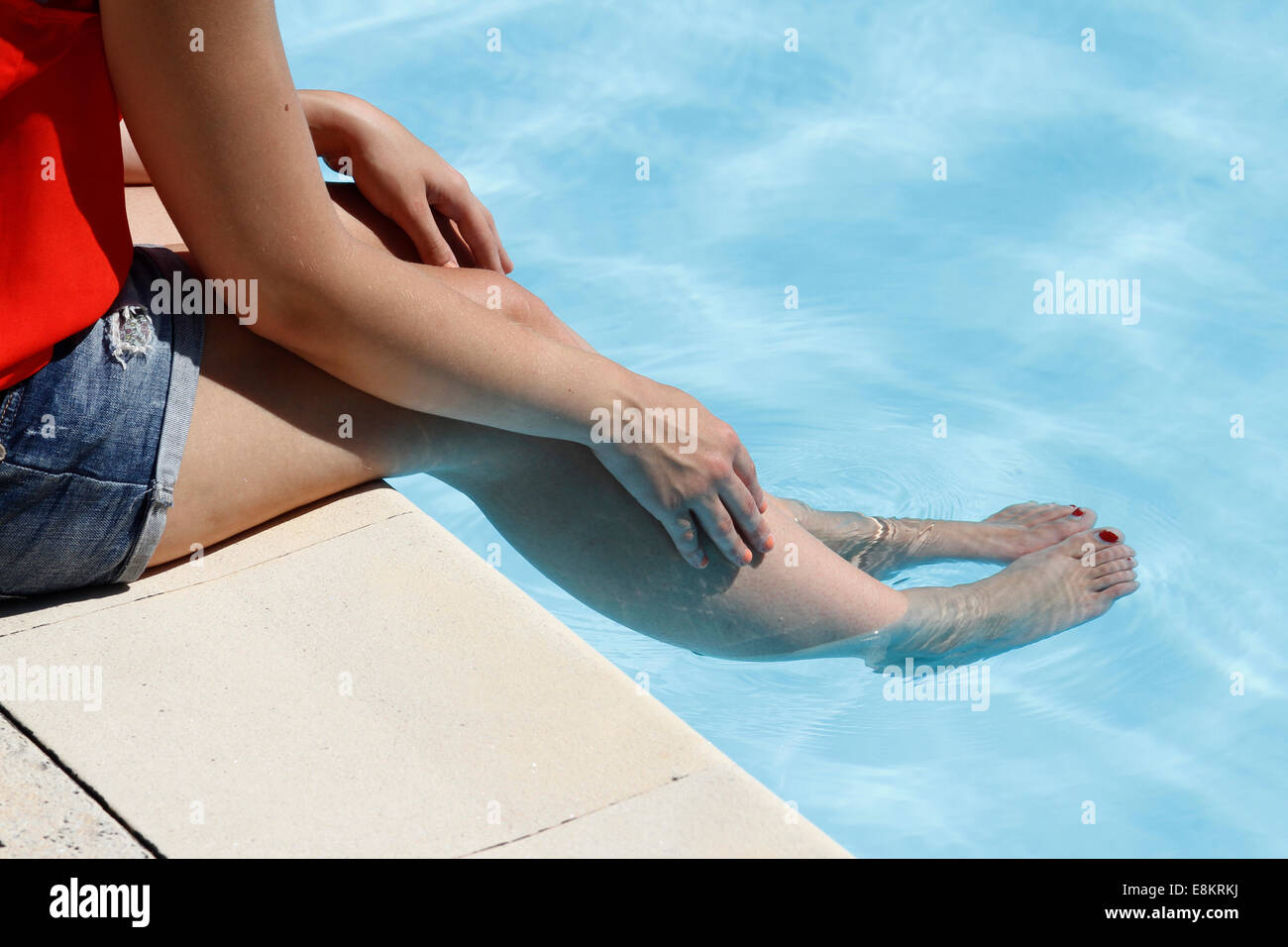 A young woman sitting on the edge of a swimming pool with her feet in the water. Stock Photo