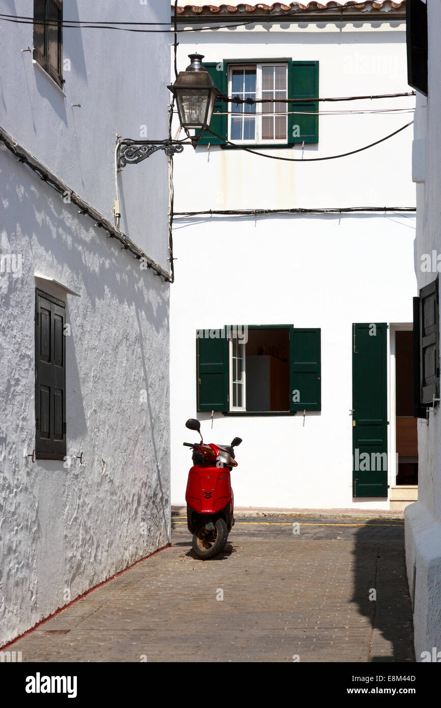 Red scooter parked in a side alley with white washed building and green wooden shutters, Formelis, Menorca, Spain Stock Photo