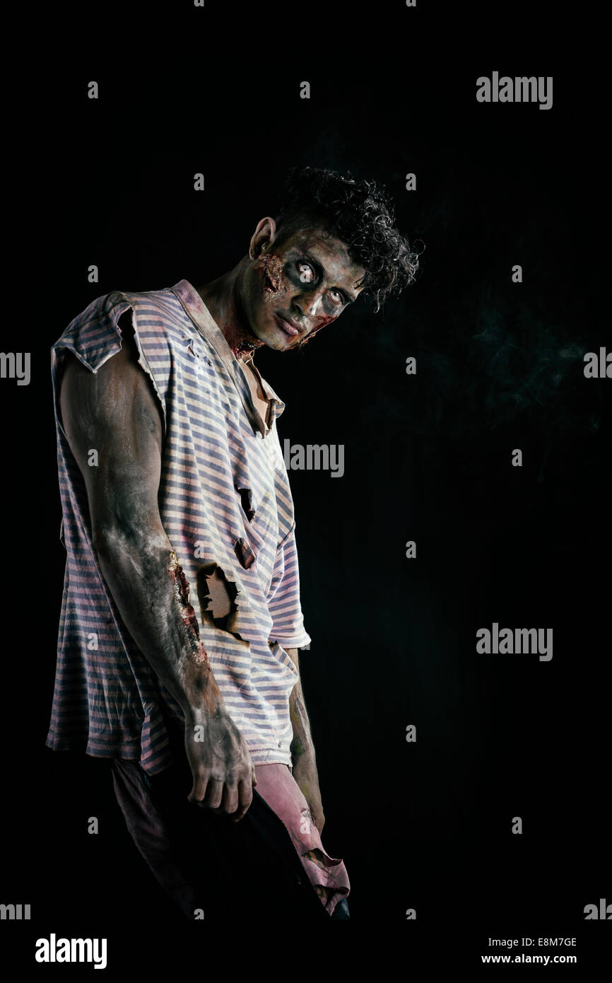 Male zombie standing on black background, with one white eye, looking at camera Stock Photo
