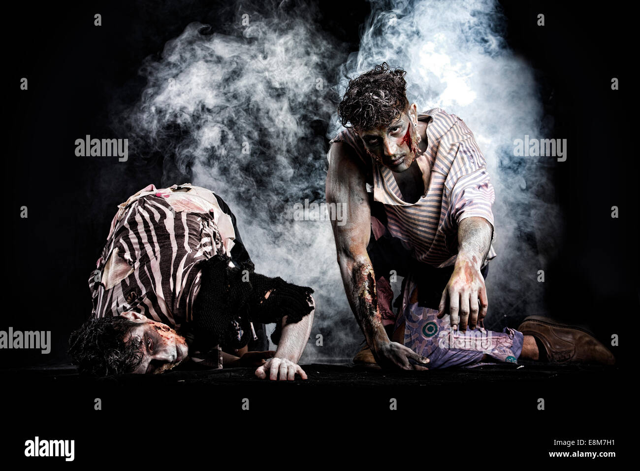 Two male zombies crawling on their knees, on black smoky background, looking at camera. Halloween theme Stock Photo