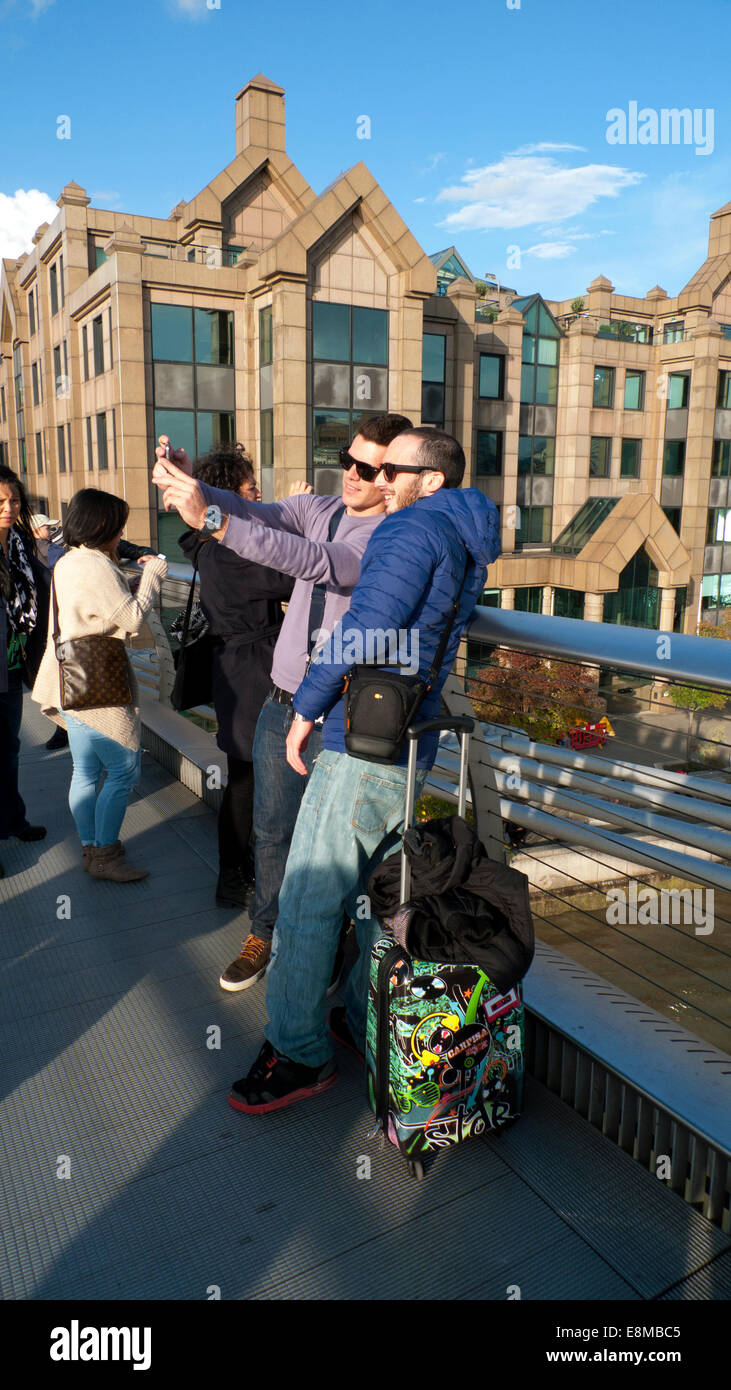 Millennium Bridge, London UK. 10th October 2014.  Two young men stop to take a selfie photo in the autumn sunshine as they cross the Millennium  or 'wobbly' Bridge late on Friday afternoon.  The forecast for London tomorrow is for a mixture of scattered thundery showers and sunny spells in the afternoon. Credit:  Kathy deWitt/Alamy Live News Stock Photo