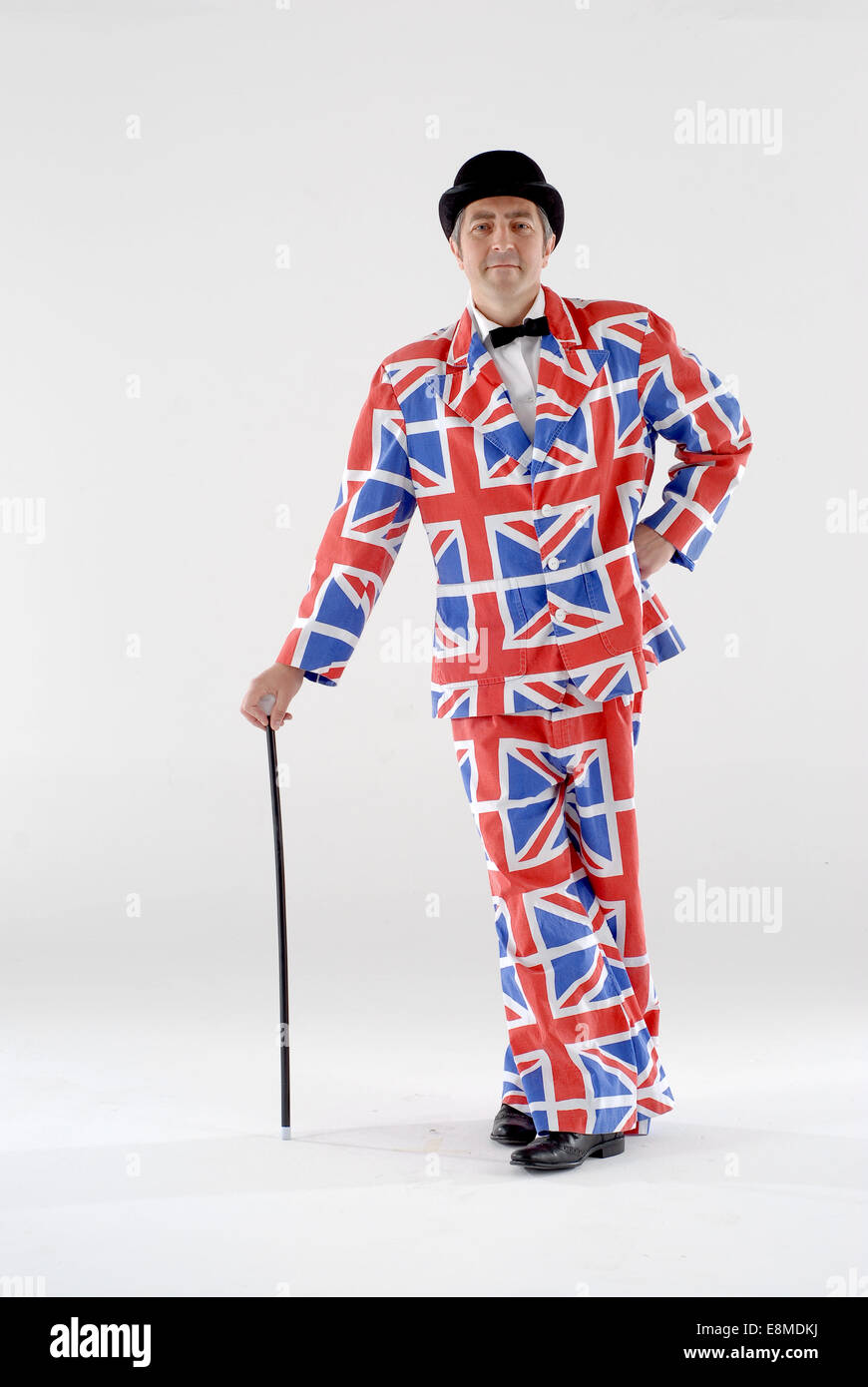 Man dressed in fancy dress comedy costume in union jack suit with bowler hat, bow tie and cane shot in a white studio. Stock Photo