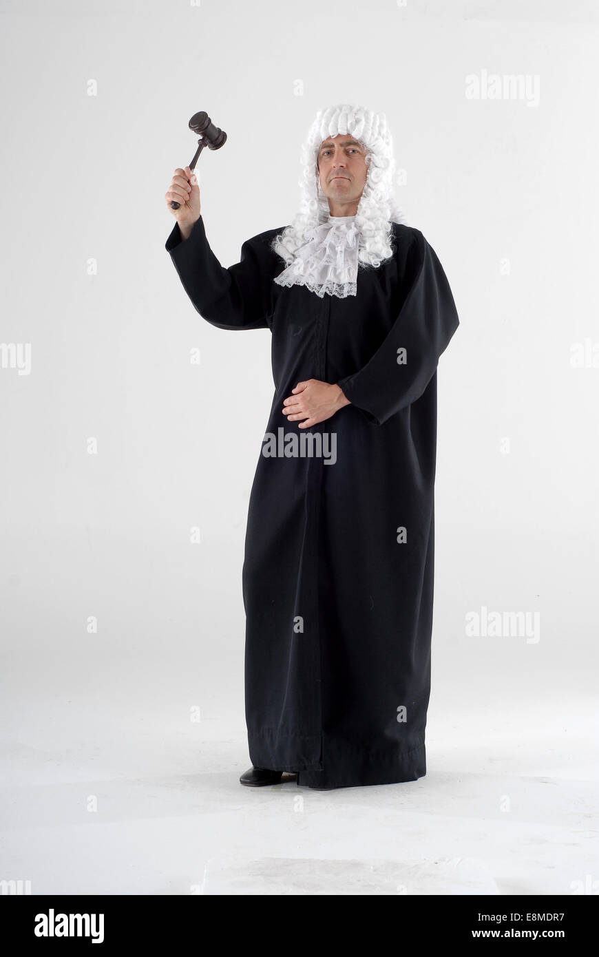 man in fancy dress comedy costume as an english judge, with wig, gown and gavel shot against a white background Stock Photo