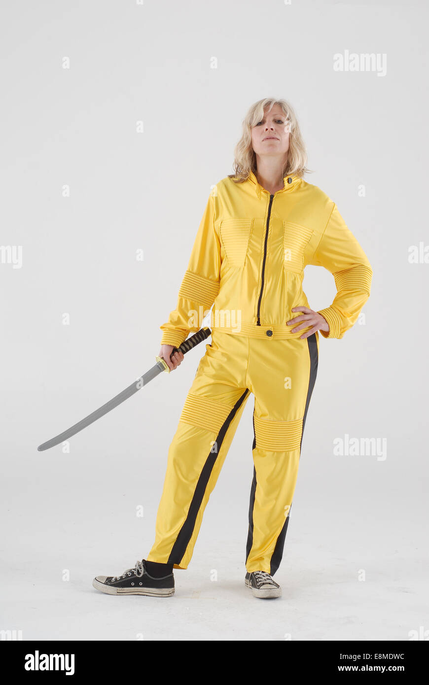 Woman in fancy dress comedy costume as The Bride from Kill Bill Movie by Tarantino with yellow jump suit / outfit, samurai sword Stock Photo