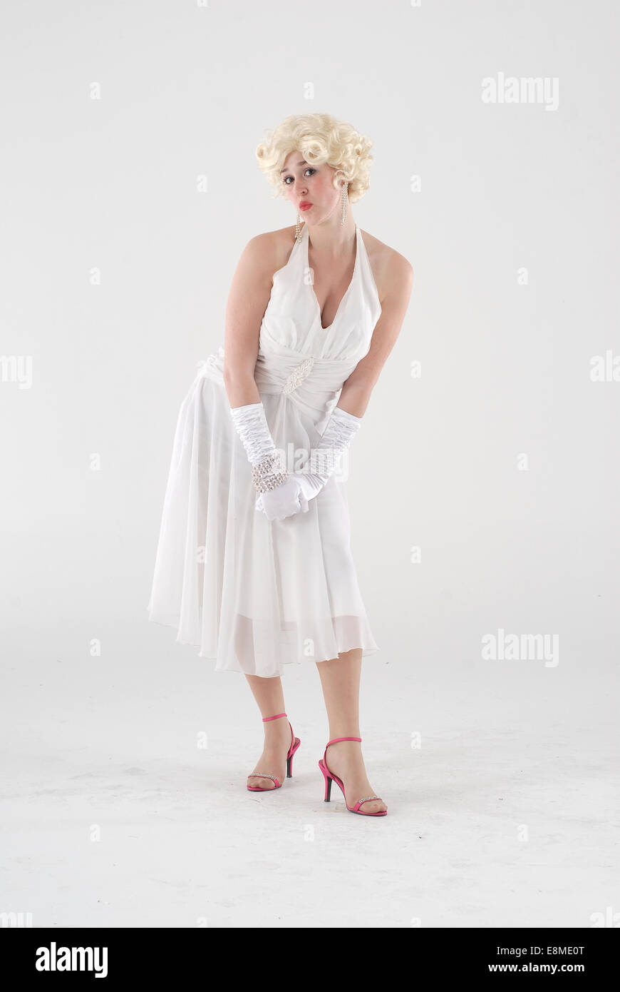 woman in fancy dress comedy costume in 1960s fashion and crazy funny outfit as marilyn monroe, with white dress and blond wig Stock Photo