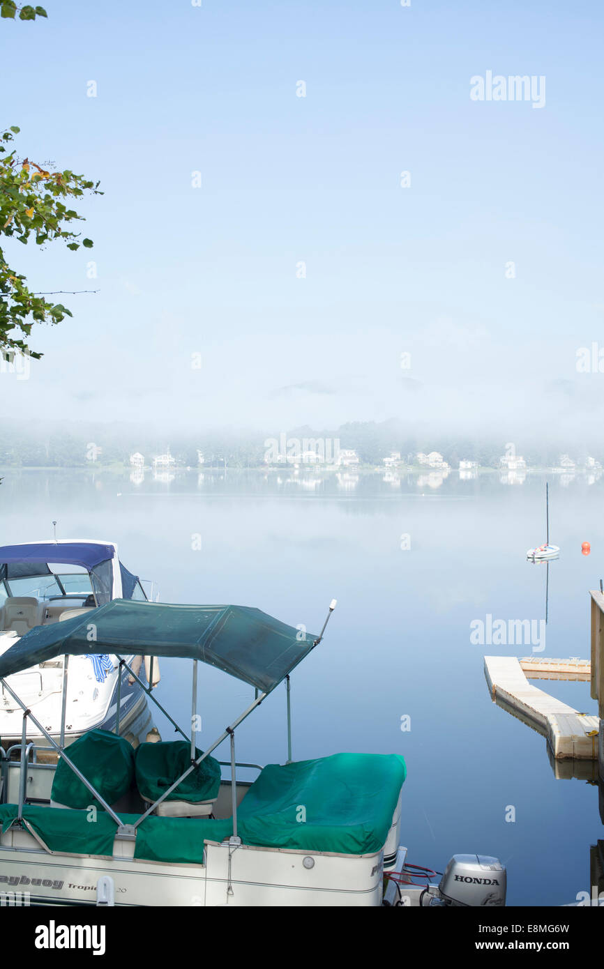 Boats are docked at a pier on Pontoosuc Lake in Pittsfield, MA on a foggy morning. Stock Photo