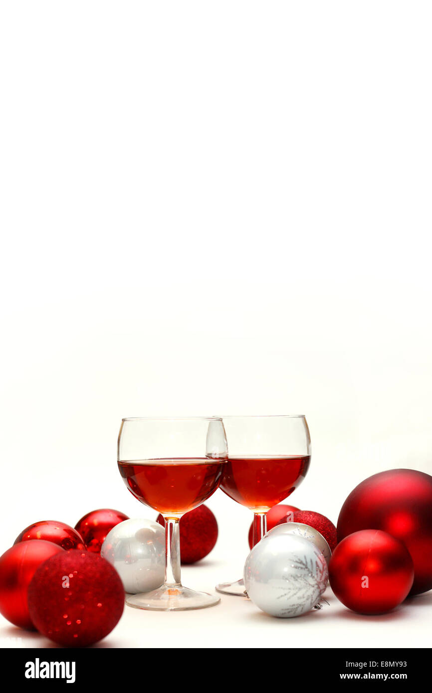 Two wine glasses filled with red wine sit on an isolated white background in surrounded by silver and red sparkling Christmas Bu Stock Photo