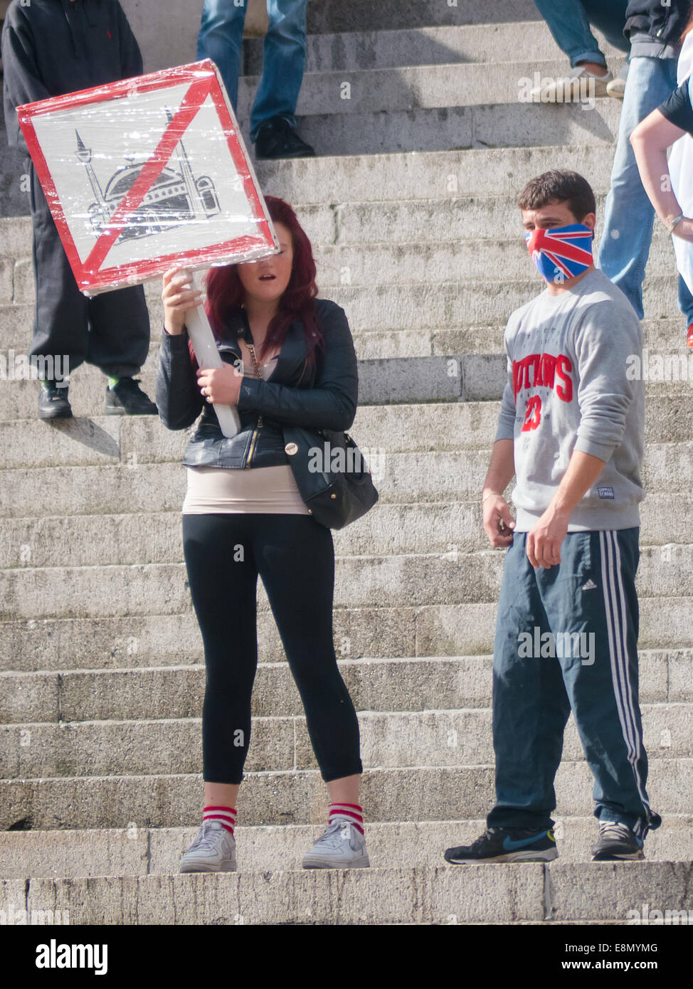 A girl holds an anti mosque sign standing beside a male with his face covered by a union flag mask during an English Defence League Protest in Portsmouth guildhall square, England Stock Photo