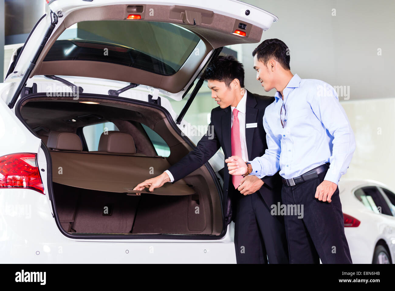 Car salesman in Asian dealership showing trunk of SUV car to customer Stock Photo