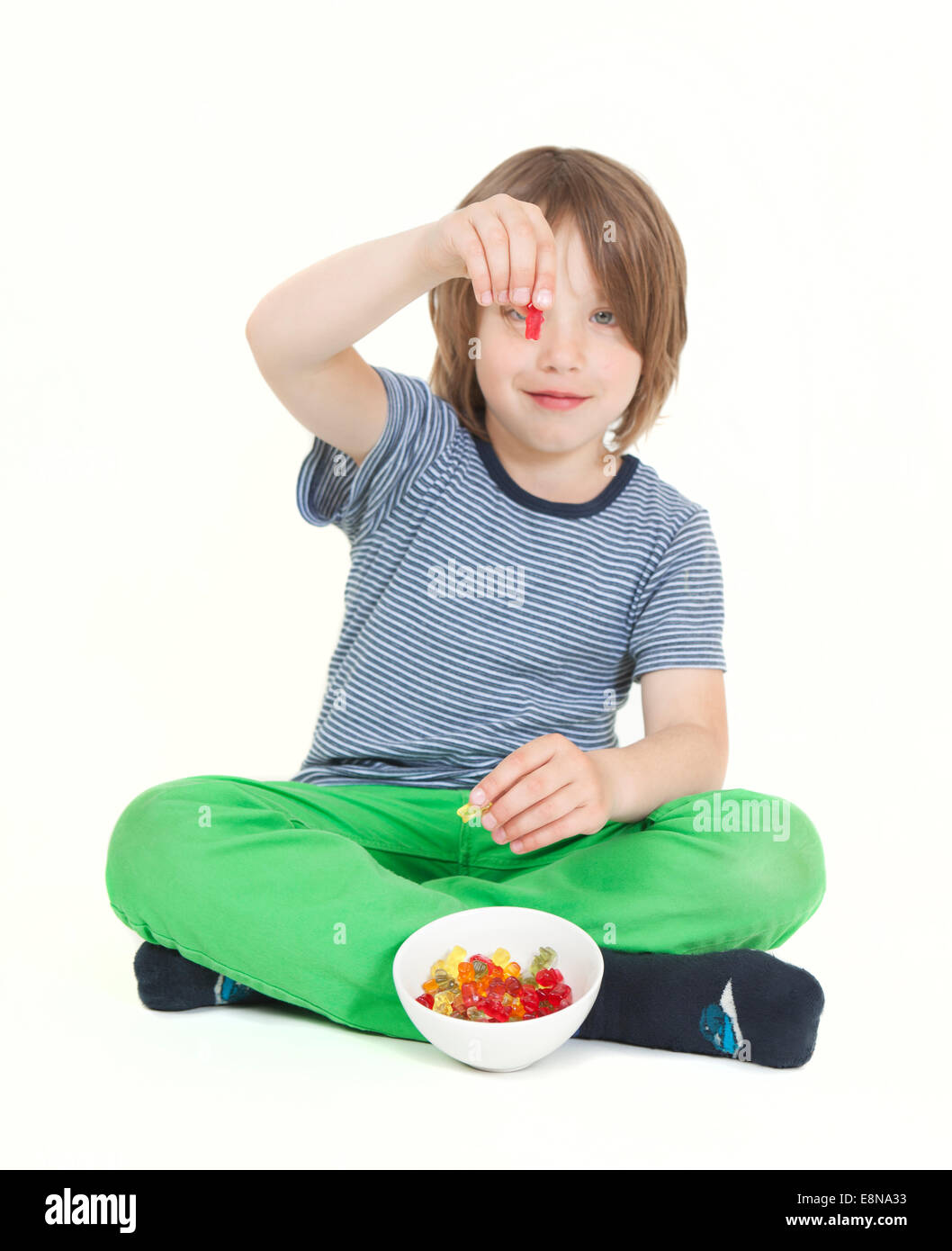 A boy with brown hair eating gummy bears, background white, isolated Stock Photo