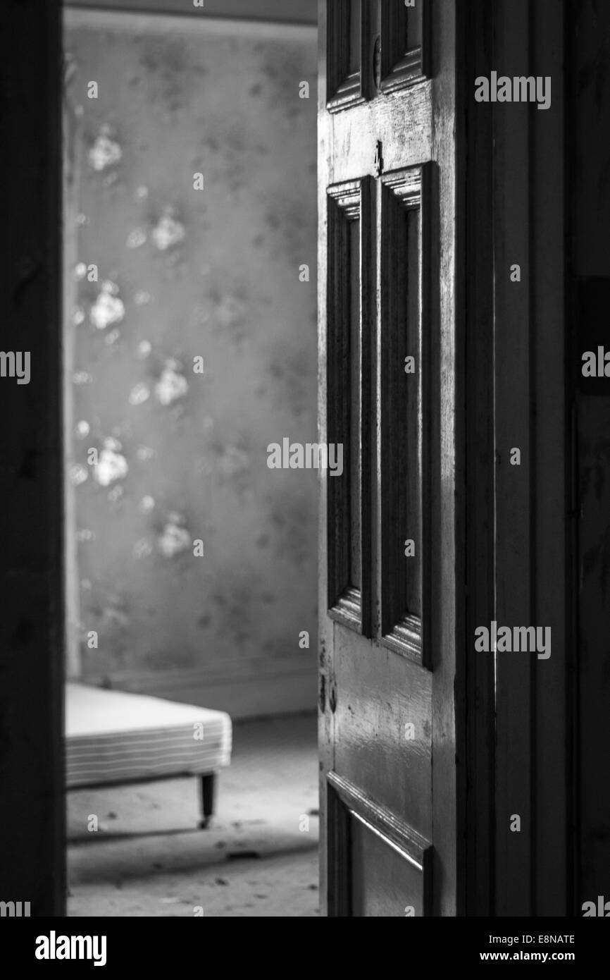 Monochrome image of an open door with missing door knob and an old room beyond Stock Photo