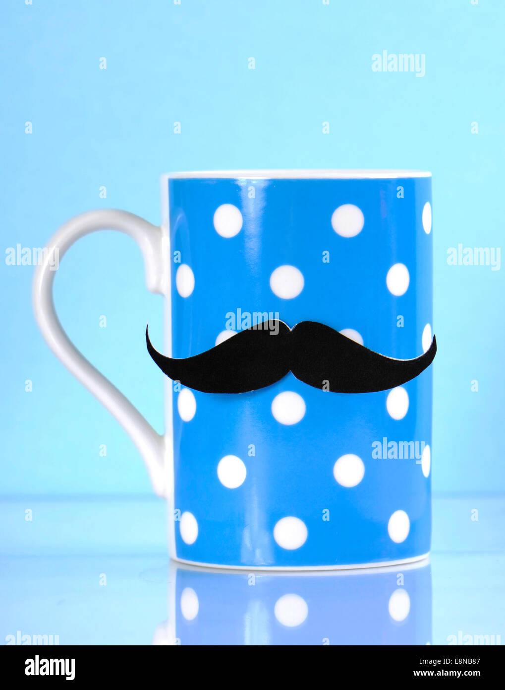 Fundraising for mens health awareness charity with mustache on blue polka dot coffee mug cup on blue background. Stock Photo