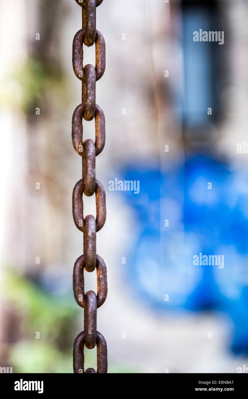 Rusty chain in focus with blue graffiti out of focus in the background Stock Photo