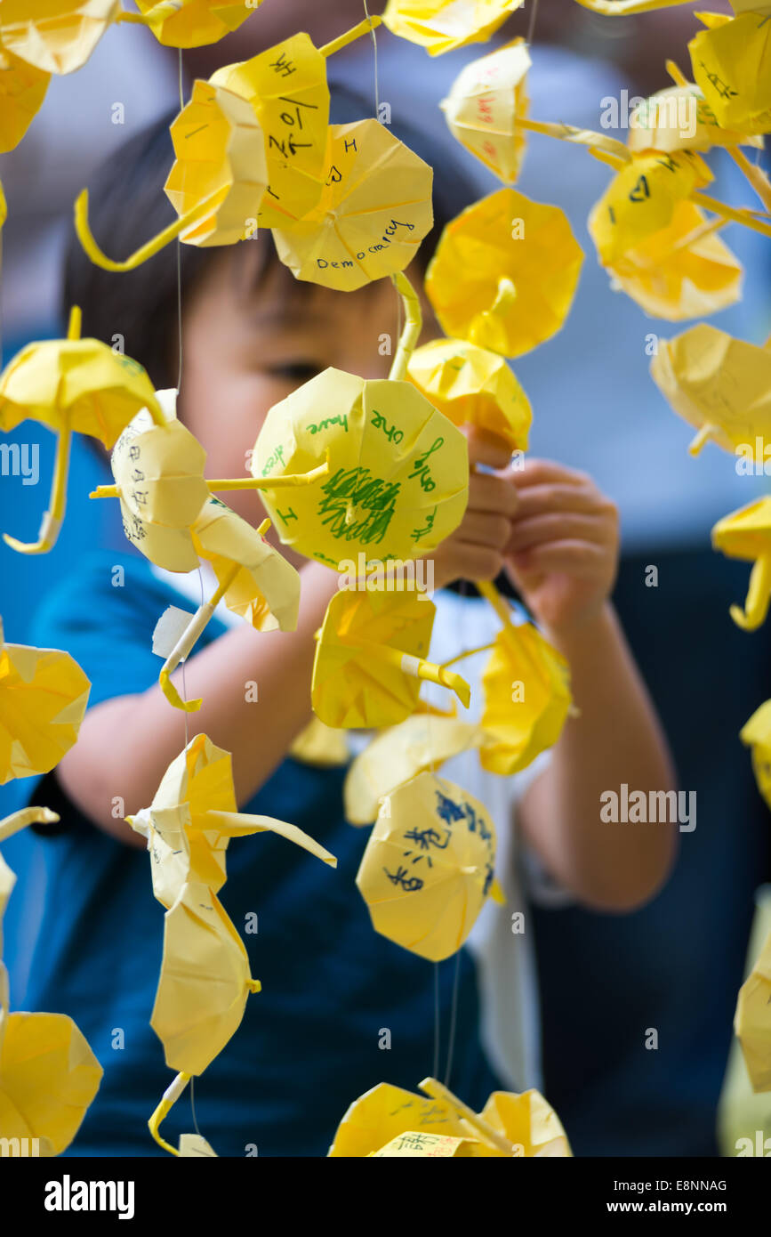 Hong Kong. 12th October, 2014. Hong Kong Protests Yellow umbrellas have become the symbol of the Hong Kong protests and are found all over the Admiralty are including  in front of the Government offices at Tamar Admiralty.  Students, pro democracy activists and other supporters learn how to make origami paper umbrellas and hang them with wishes Yellow umbrellas are the symbol of the protest.  Yellow paper umbrellas are found decorating the Admiralty protest site. Stock Photo