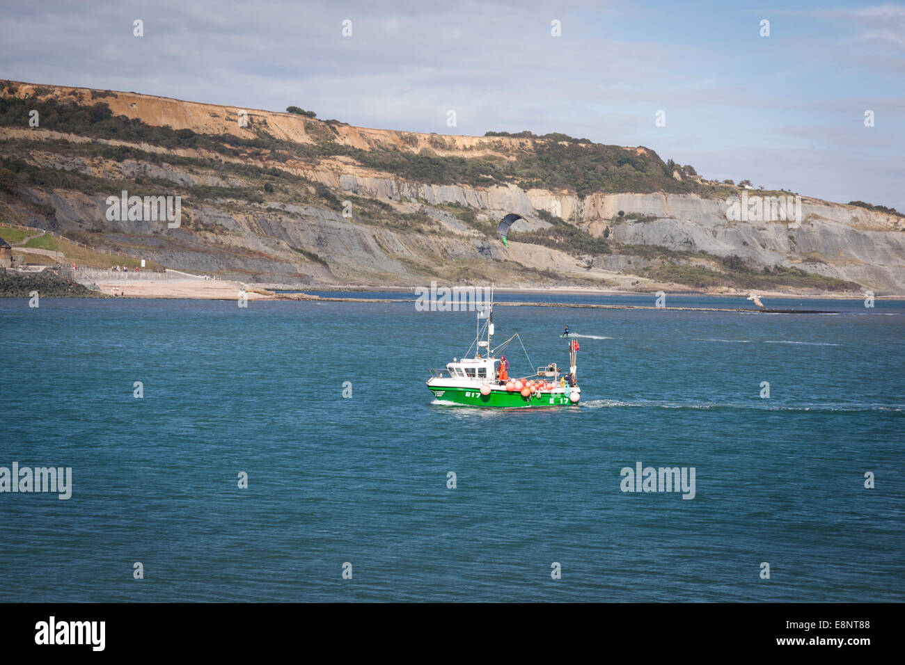 A small fishing boat returns to Lyme Regis harbour with a kite surfer ...