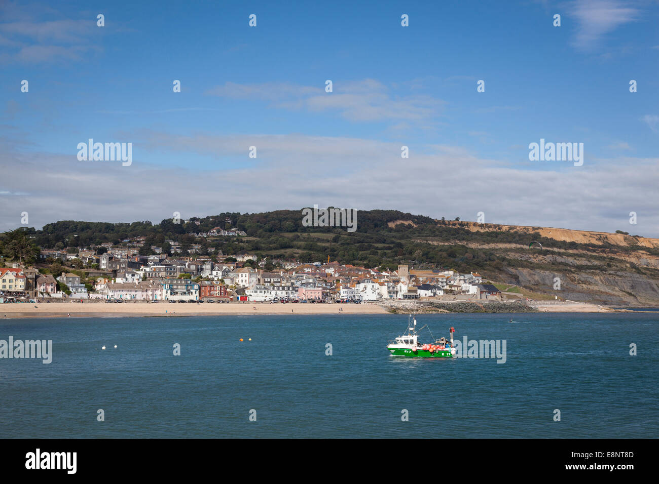 A small fishing boat returns to Lyme Regis harbour with the town of ...