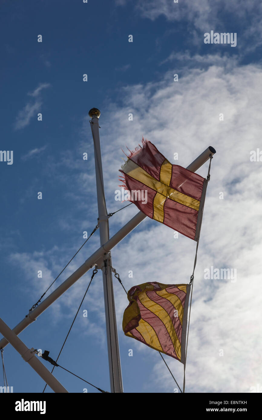 Maritime flags for R and Y (meaning proceed at slow speed), flying from a mast on a harbour wall. Stock Photo