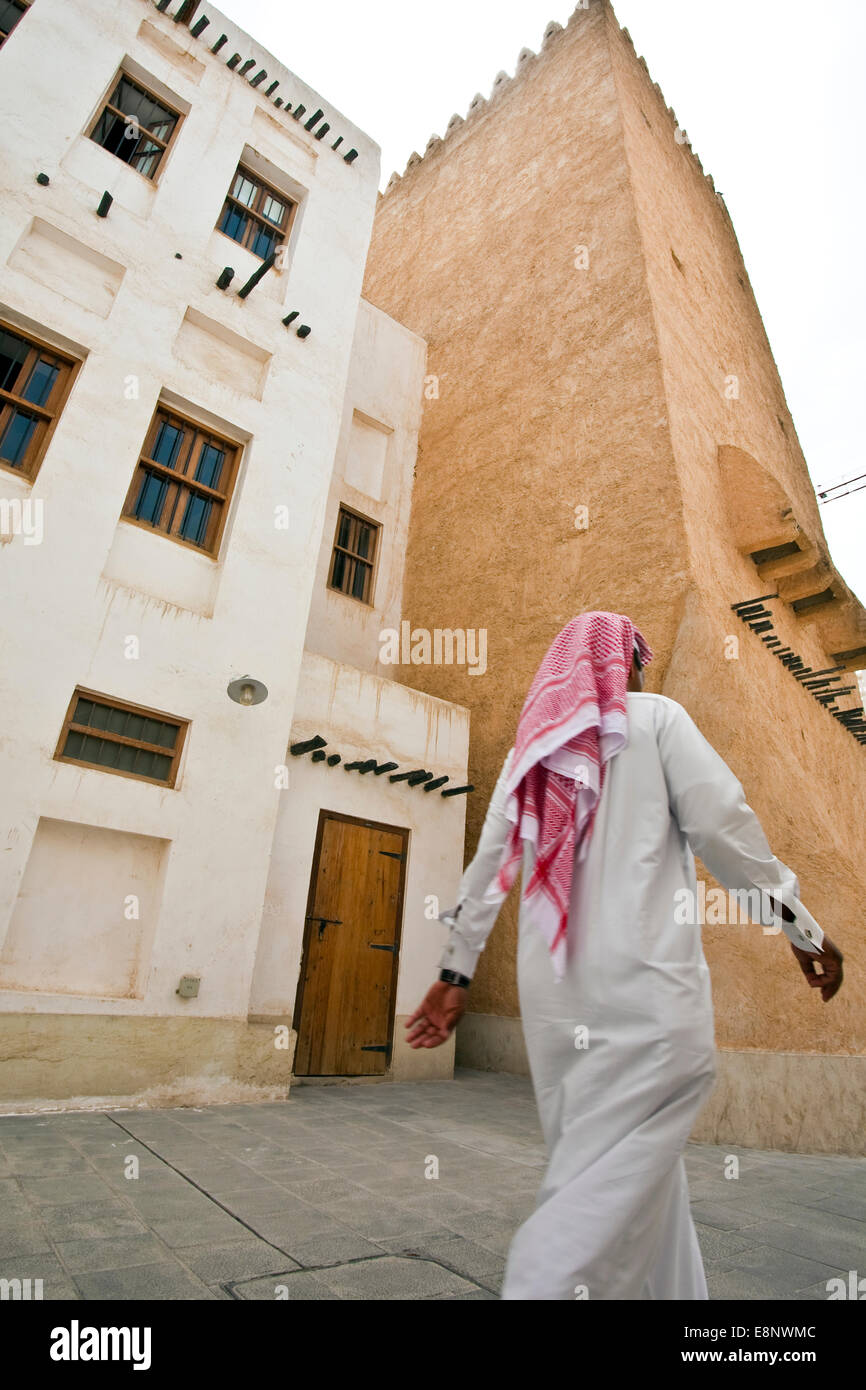 A Qatari man walking past traditional houses in the street in Doha Qatar Stock Photo