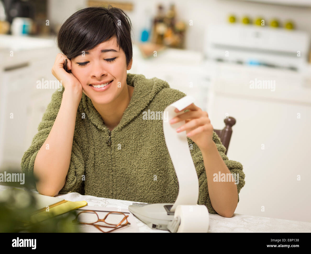 Multi-ethnic Young Woman Relieved and Smiling Over Financial Calculations in Her Kitchen. Stock Photo