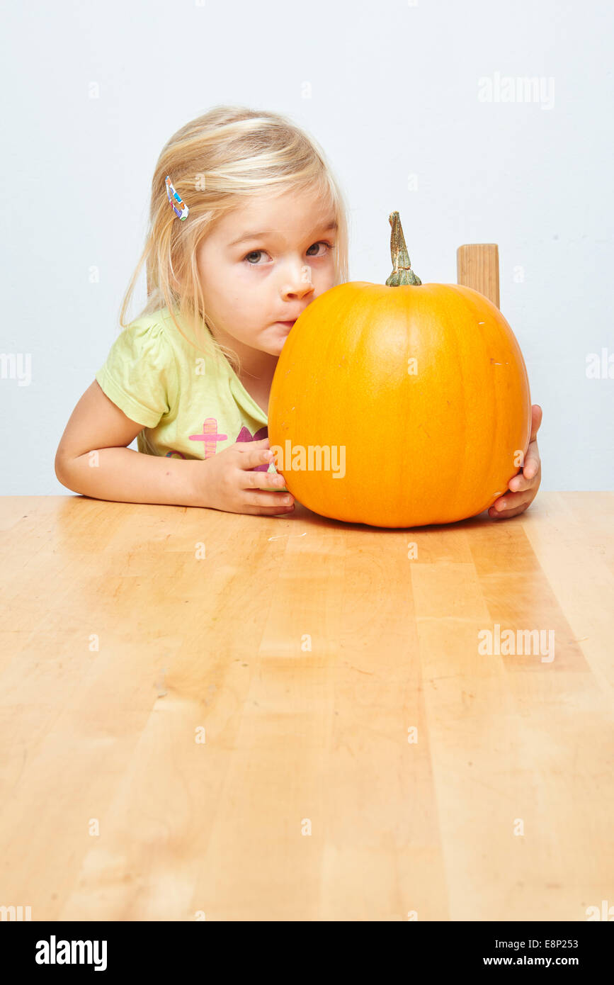 Portrait of little child blond girl sitting at a table with pumpkin, white background Stock Photo