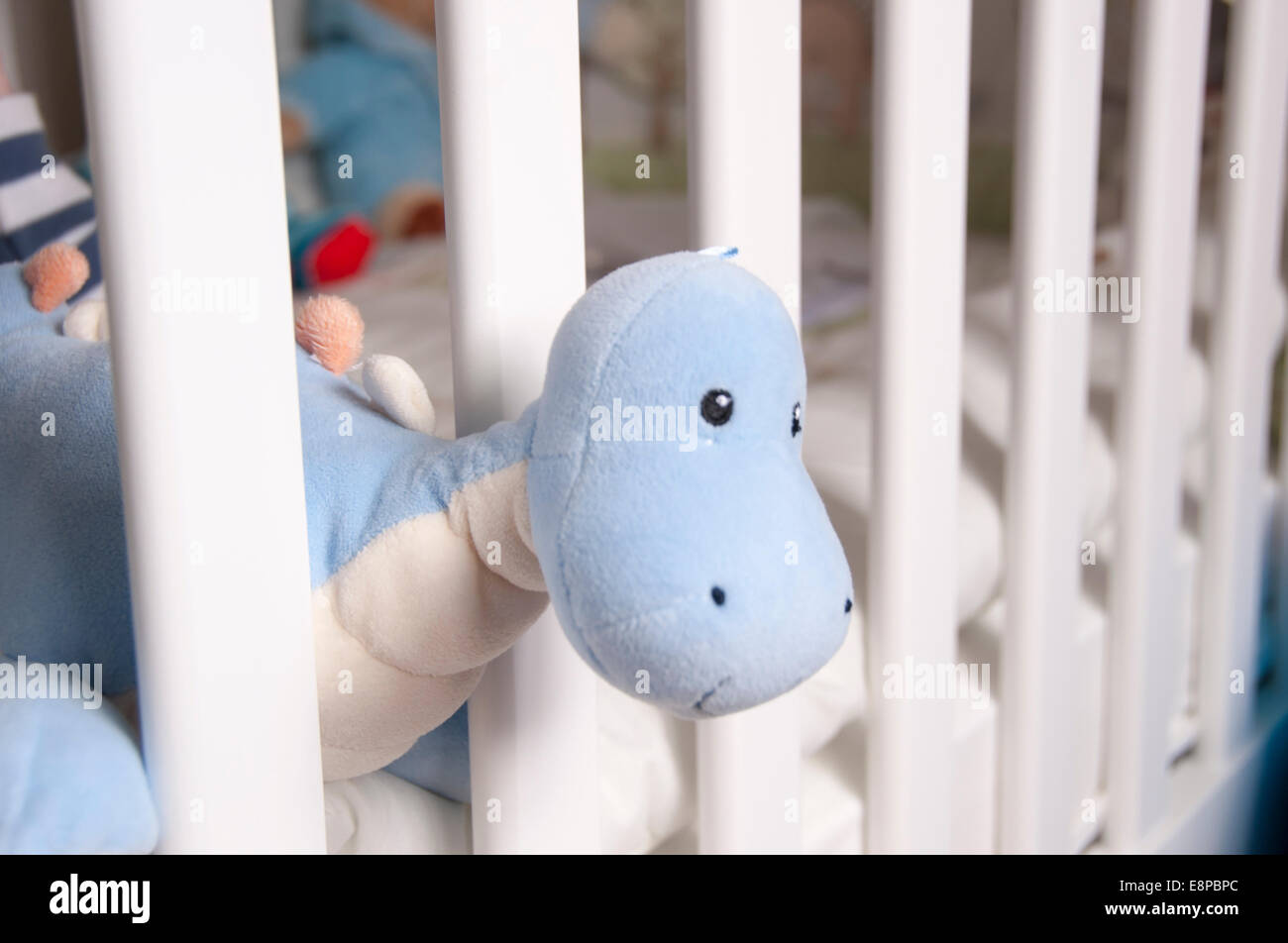 Toy dinosaur hanging out of babies crib Stock Photo