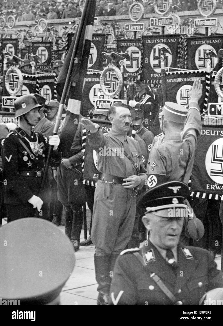 Nuremberg Rally 1937 in Nuremberg, Germany - The new standards are consecrated with the 'Blood Flag' by Adolf Hitler during the great roll call of the Sturmtruppe (SA), Schutzstaffel (SS), National Socialist Motor Corps (NSKK) and National Socialist Flyers Corps (NSFK) at Puitpoldarena at the Nazi party rally grounds. The 'Blood Flag' bearer Jakob Grimminger stands behind Hitler. New standards of SA and SS were 'consecrated' by touching them to the 'Blood Flag', which supposedly was carried in the failed Beer Hall Putsch. (Flaws in quality due to the historic picture copy) Photo: Berliner Ver Stock Photo