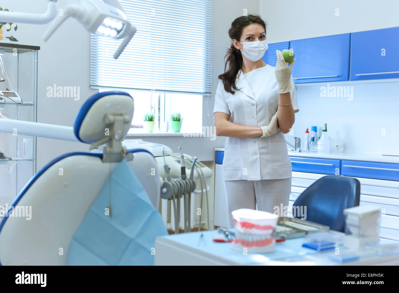 Dentist woman in mask at stomatology office holding green apple. Health