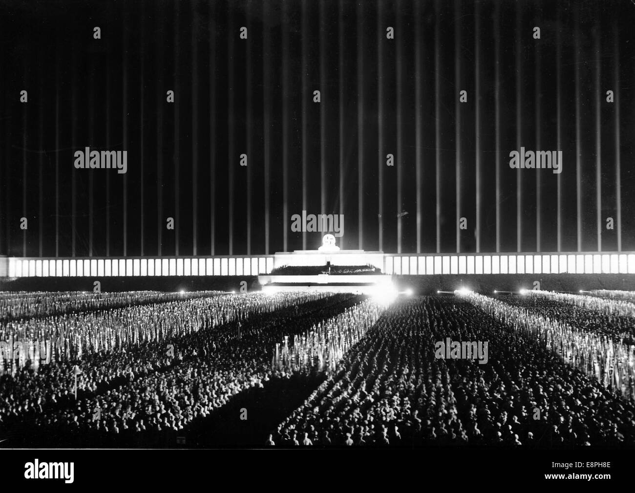 Nuremberg Rally 1937 in Nuremberg, Germany - View of the roll call of the political leaders of the Nazi party (NSDAP) on Zeppelin Field at the Nazi party rally grounds. Original propaganda text! from Nazi news reporting on the back of the picture: 'The great roll call of the political leaders took place this evening, 110,000 of whom had fallen into formation in twelve enormous blocks. The searchlights suddenly flared up and created a fantastic colour symphony in an overwhelming rapture of light in brown and red and white, in glittering silver and gold. Our picture: The magically illuminated Ze Stock Photo