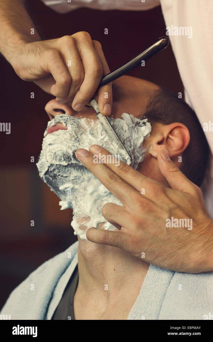 Young man getting an oldfashioned shave at the barber shop. Closeup