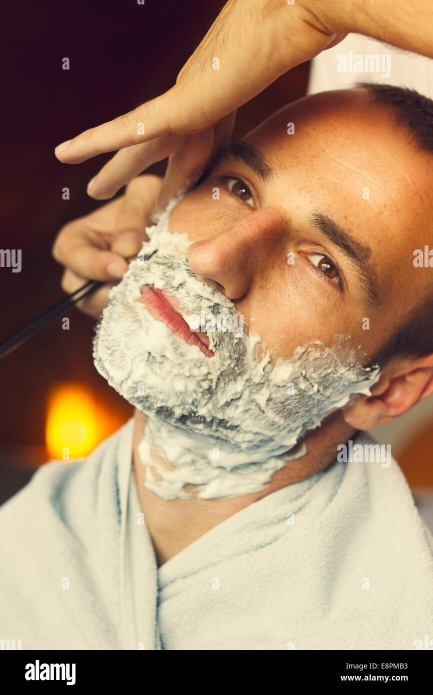Young man getting an oldfashioned shave at the barber shop. Closeup