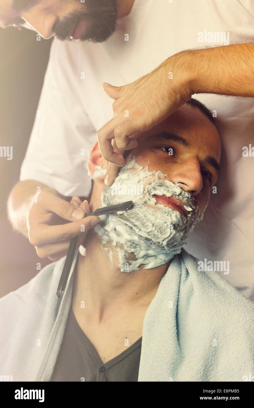 Young man getting an oldfashioned shave at the barber shop. Closeup