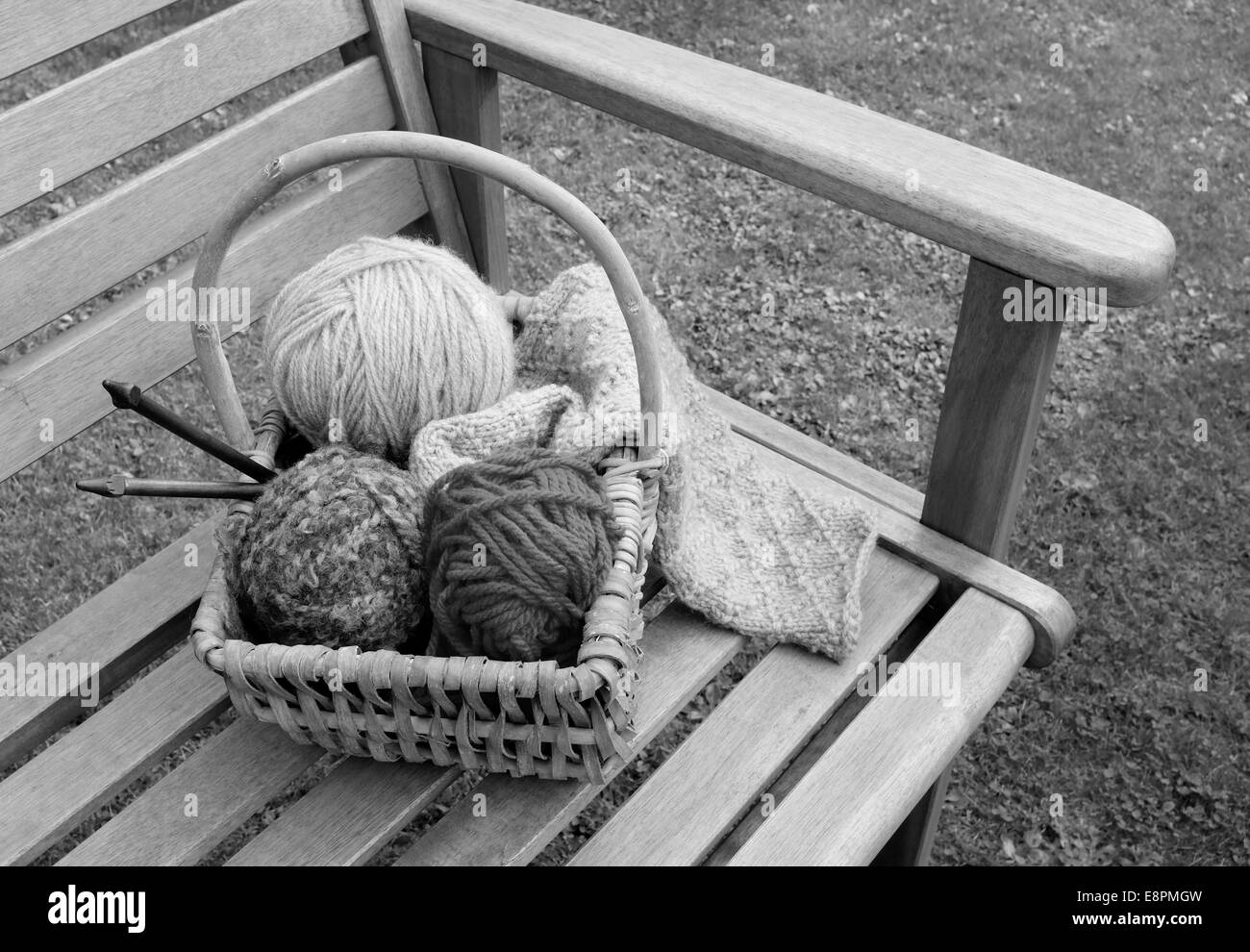 Craft basket of patterned knitting, balls of wool and wooden needles on a garden bench - monochrome processing Stock Photo