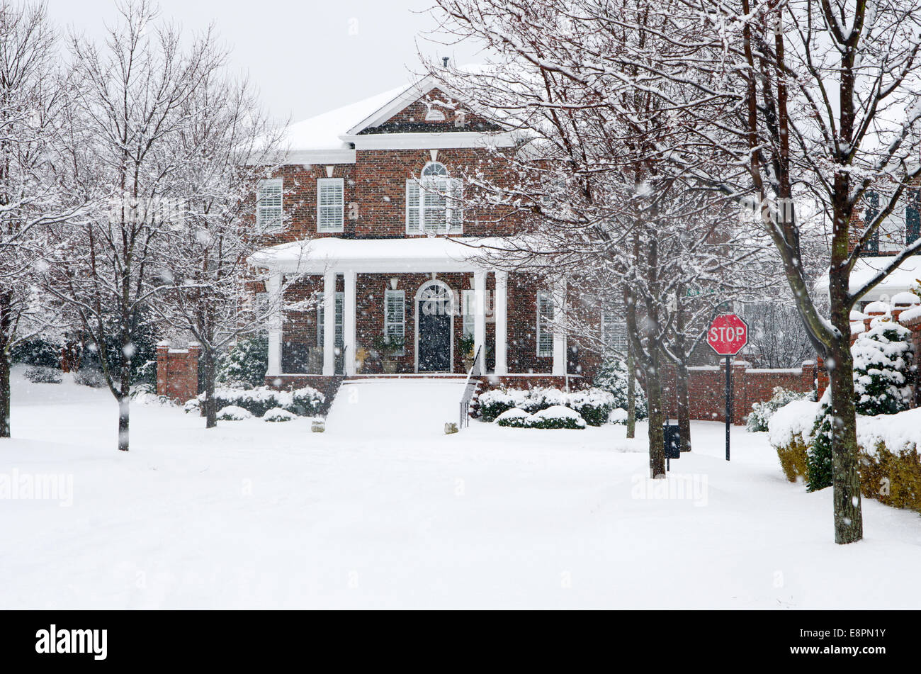 A traditional, brick home is captured during a snow storm in this beautiful, Winter scene. Stock Photo