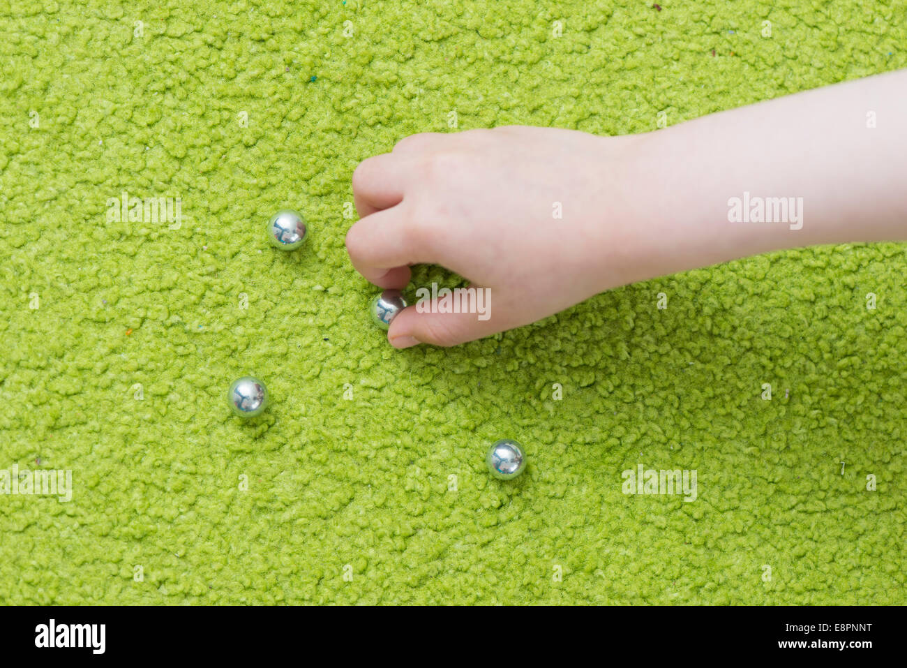 Hand of child playing with steel marbles on green carpet. Stock Photo