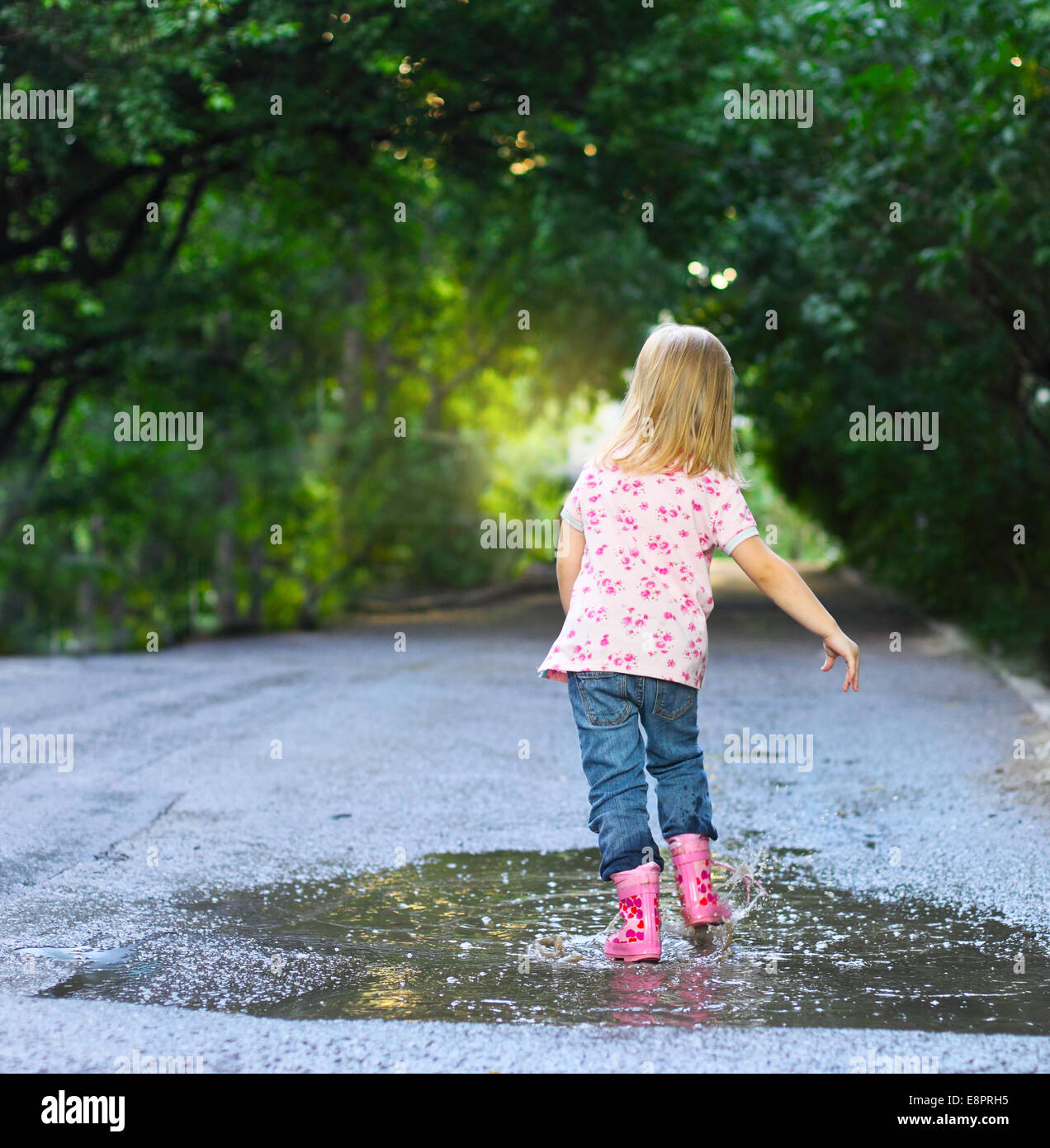 Cute little girl wearing rain boots jumping into a puddle Stock Photo ...