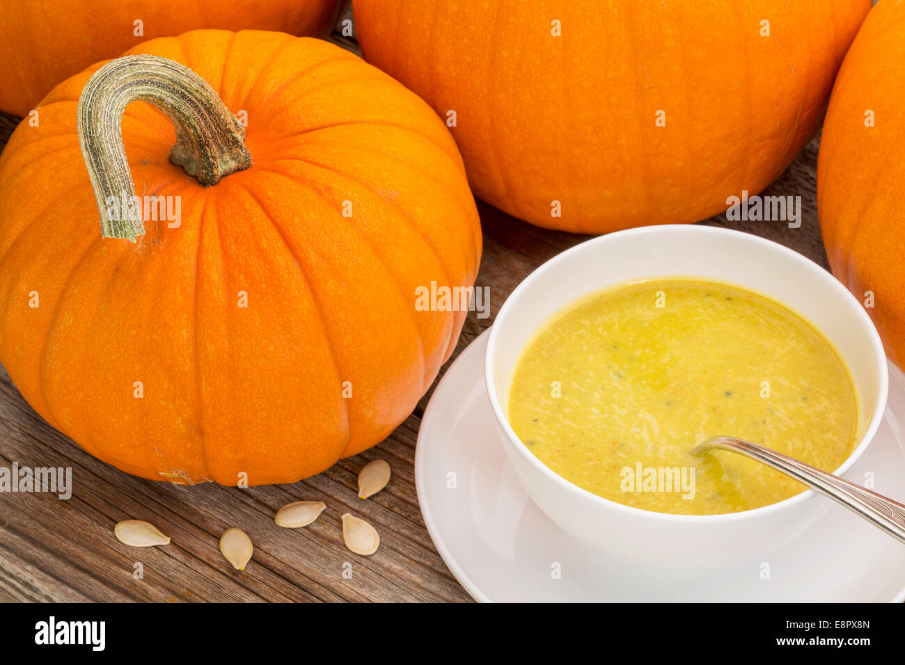 pumpkin cream soup - a bowl surrounded by pumpkins on a rustic wooden table Stock Photo