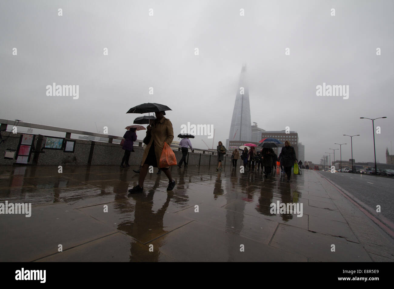 People walk over London Bridge with  Shard in background in rain, fog and mist Stock Photo