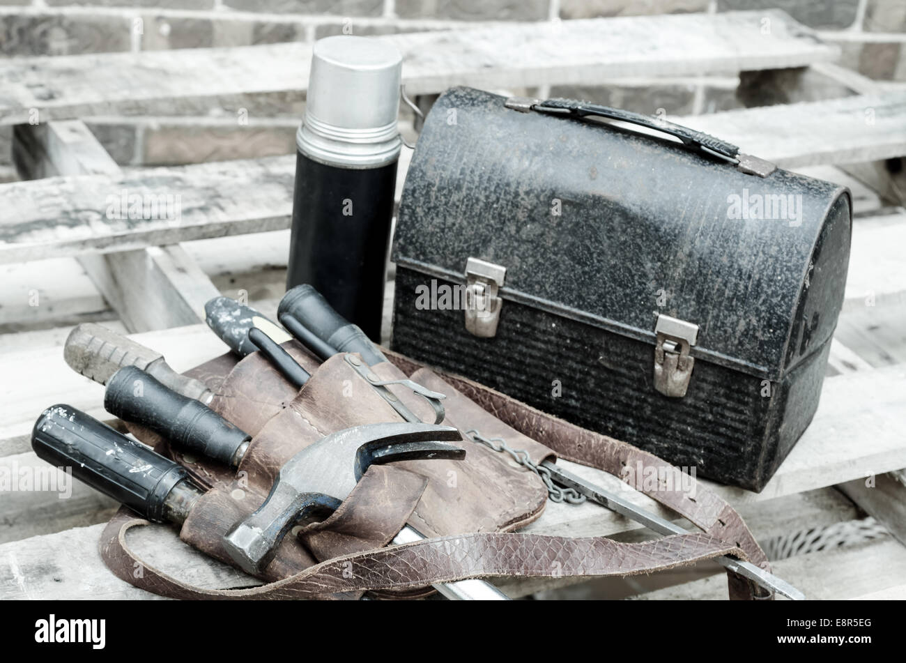 Construction worker's lunch break with lunch pail, beverage container, tool belt, hammer, screwdrivers, and wrenches on wooden p Stock Photo