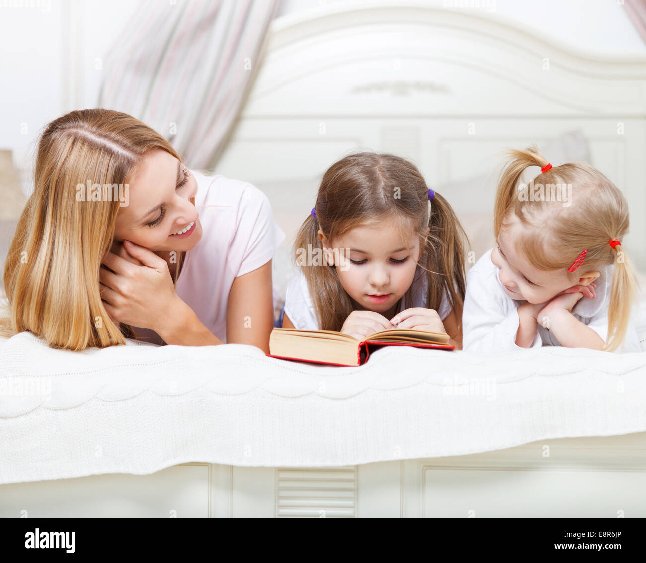 Mother and her daughters reading bed time story book in bed Stock Photo