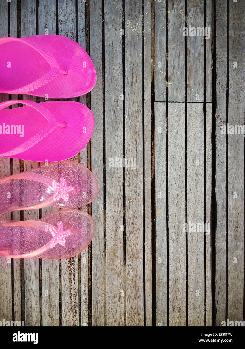Brightly colored pink flip-flops of a mother and daughter on wood ...