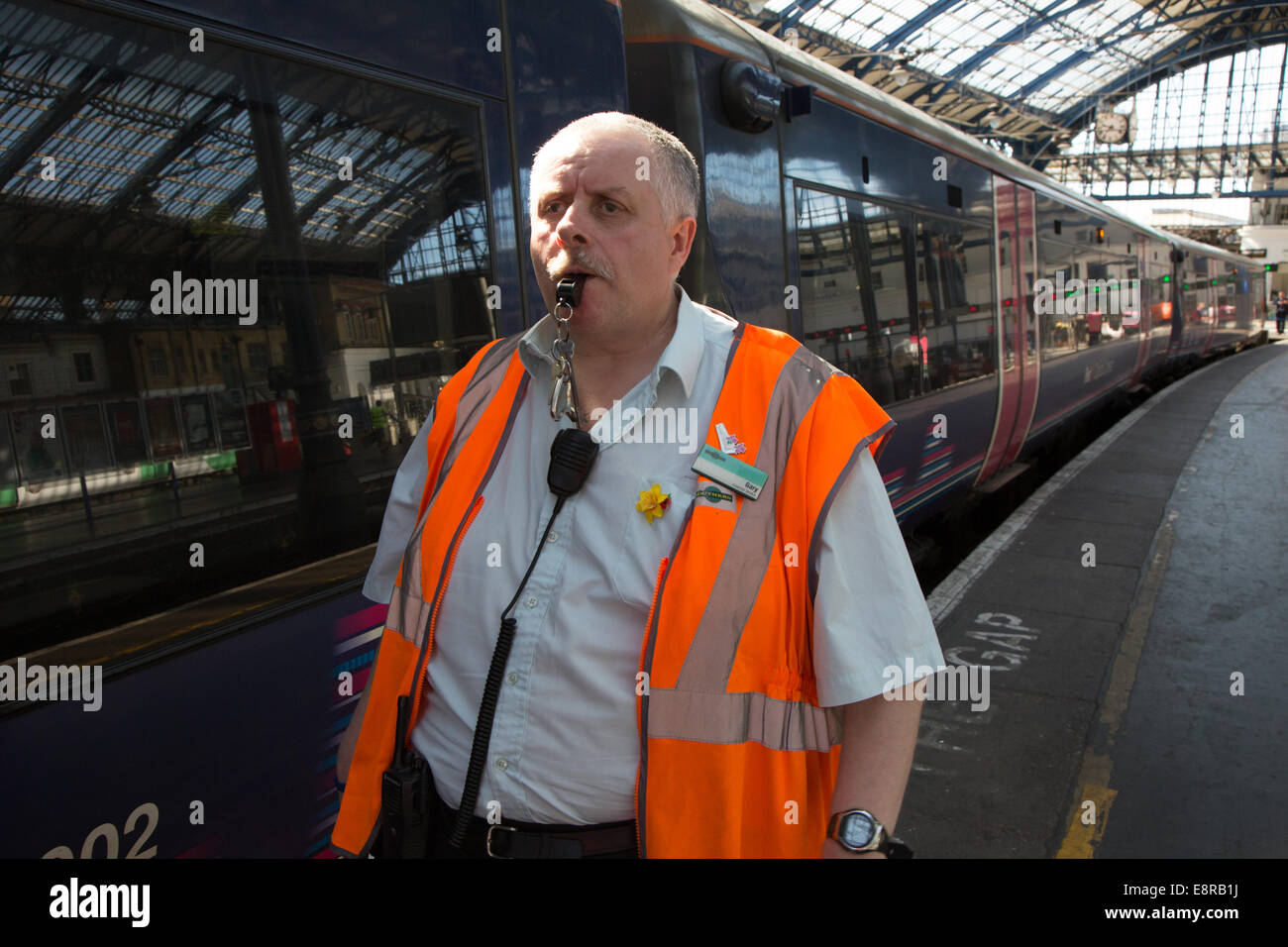 A Signal Man at a railway station prepares to blow his whistle to notify the driver to pull away. At Brighton Train Station Stock Photo