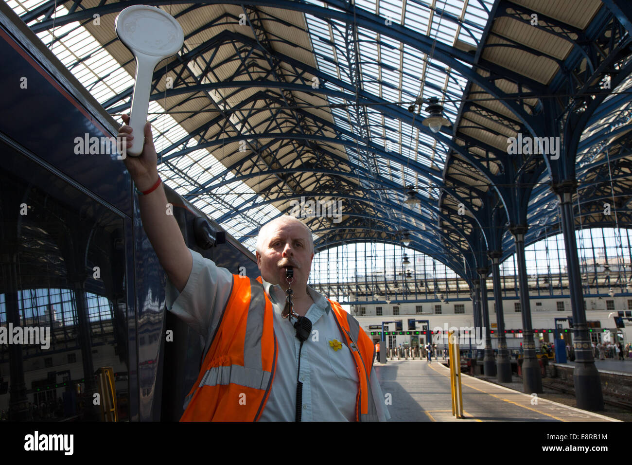 A Signal Man at a railway station prepares to blow his whistle to notify the driver to pull away. At Brighton Train Station Stock Photo