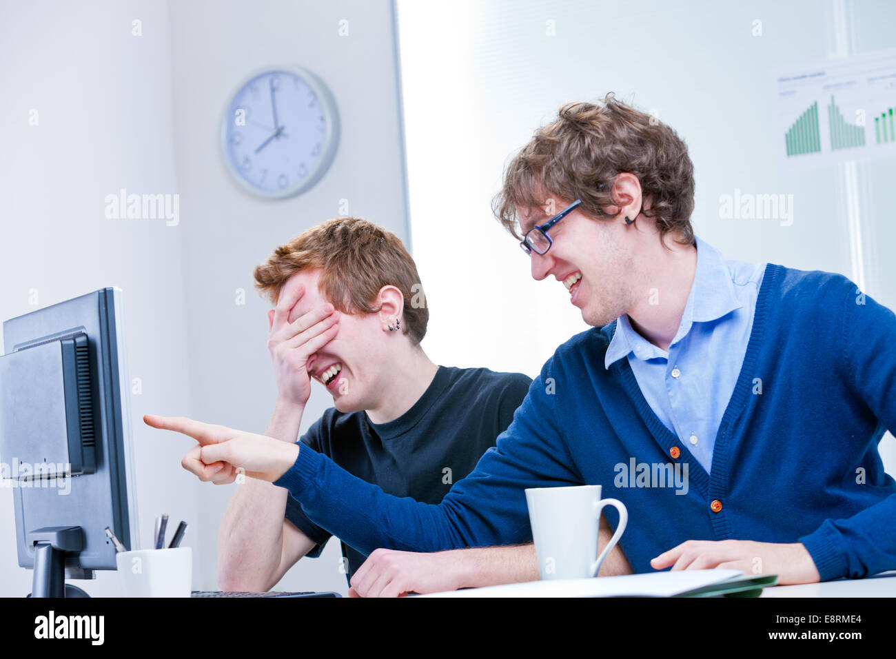 a couple of two young office workers laugh at what is happening on the screen Stock Photo