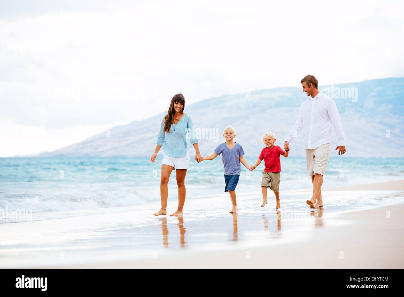 Happy Young Family Walking Down the Beach at Sunset Stock Photo