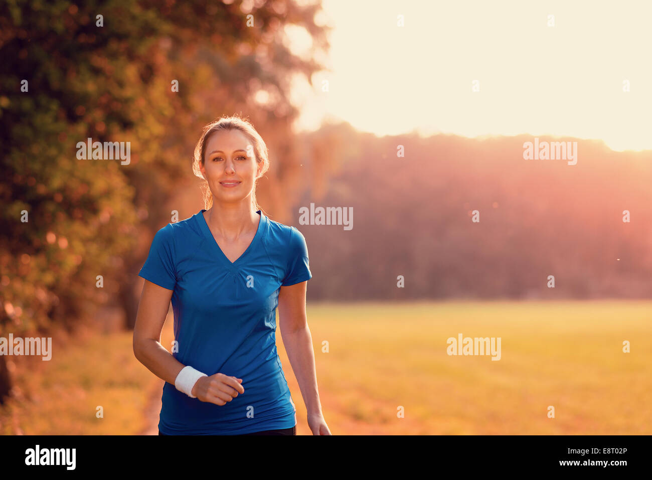 Attractive active young woman out exercising in glowing morning light on a country path through woodland and fields in a health, Stock Photo