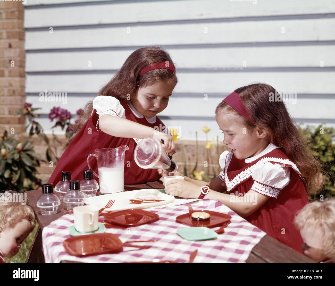 1960s TWIN GIRLS HAVING A TEA PARTY MILK AND COOKIES Stock Photo