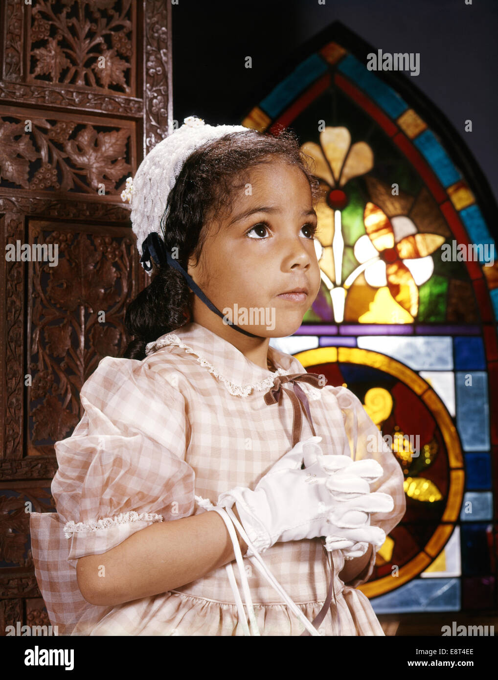 1960s AFRICAN AMERICAN GIRL IN CHURCH BY STAINED GLASS WINDOW